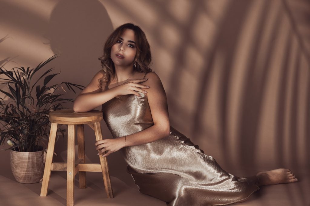 Artistic fashion portrait of a woman in a golden satin dress with palm shadows in the background. Photographed by a professional photographer in Luxembourg.