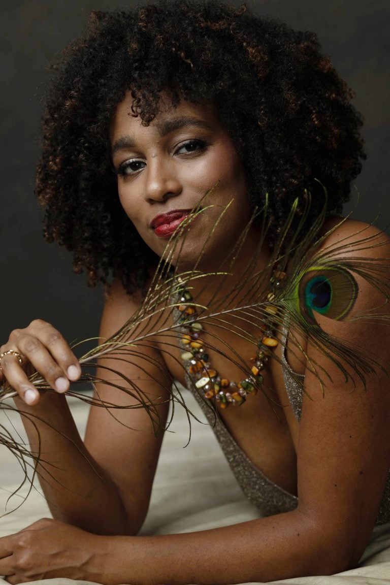 Elegant woman holding a peacock feather and wearing colorful jewelry in studio