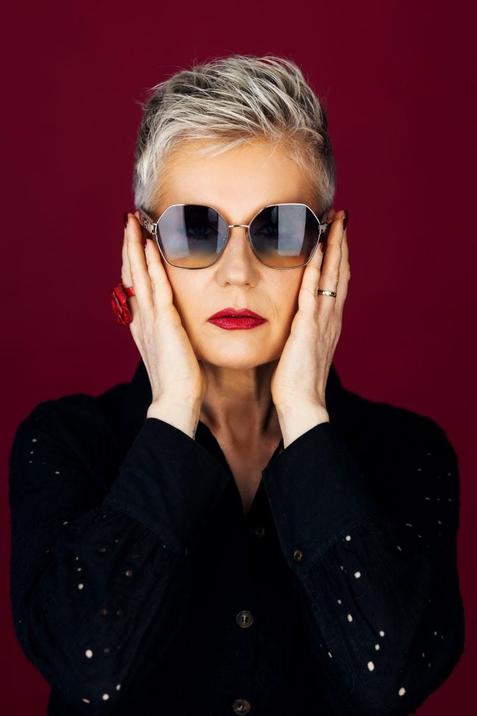 Bold older woman in sunglasses and red lipstick posing in front of red backdrop