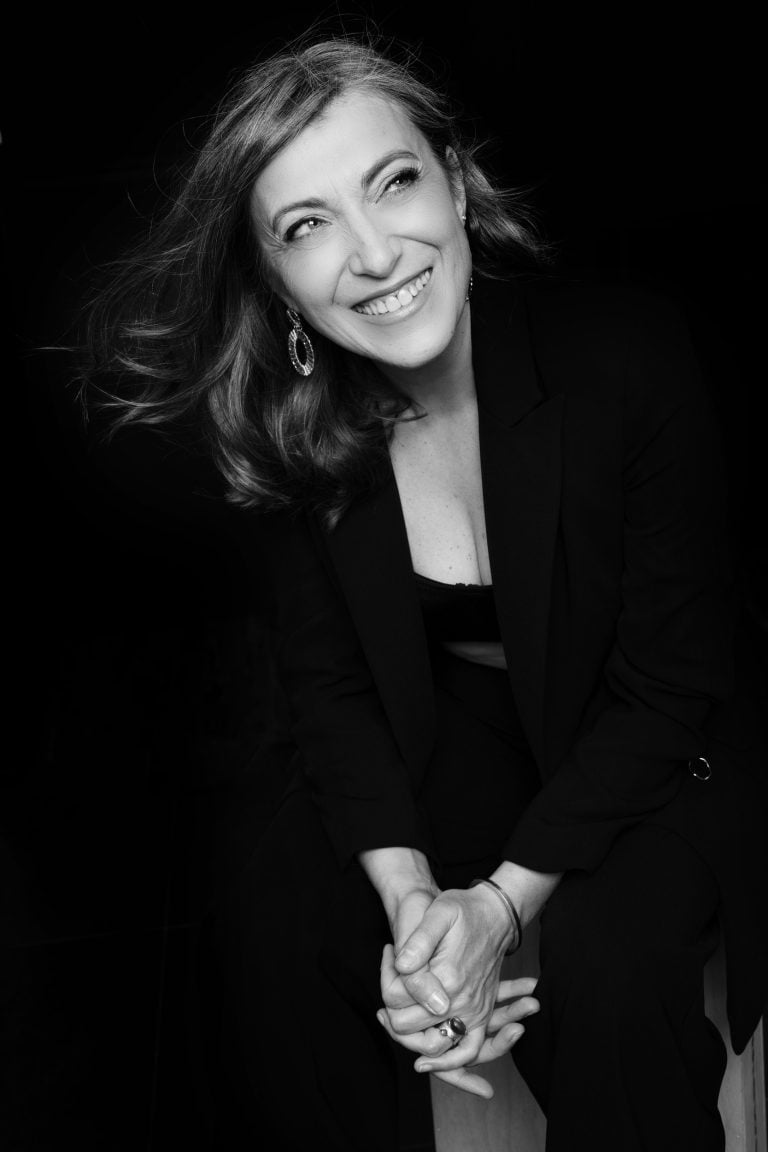 Black and white studio portrait of Christelle with flowing hair, smiling in a black blazer