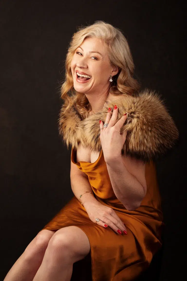 Joyful portrait of a mature woman in a golden satin dress with fur shawl, captured in a Luxembourg studio.