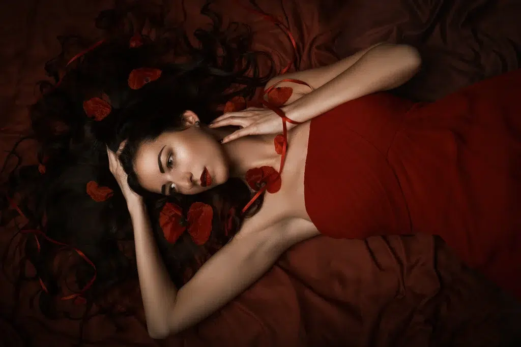 Artistic portrait of a woman in a red dress lying on fabric with poppy flowers in her hair, Luxembourg studio session.