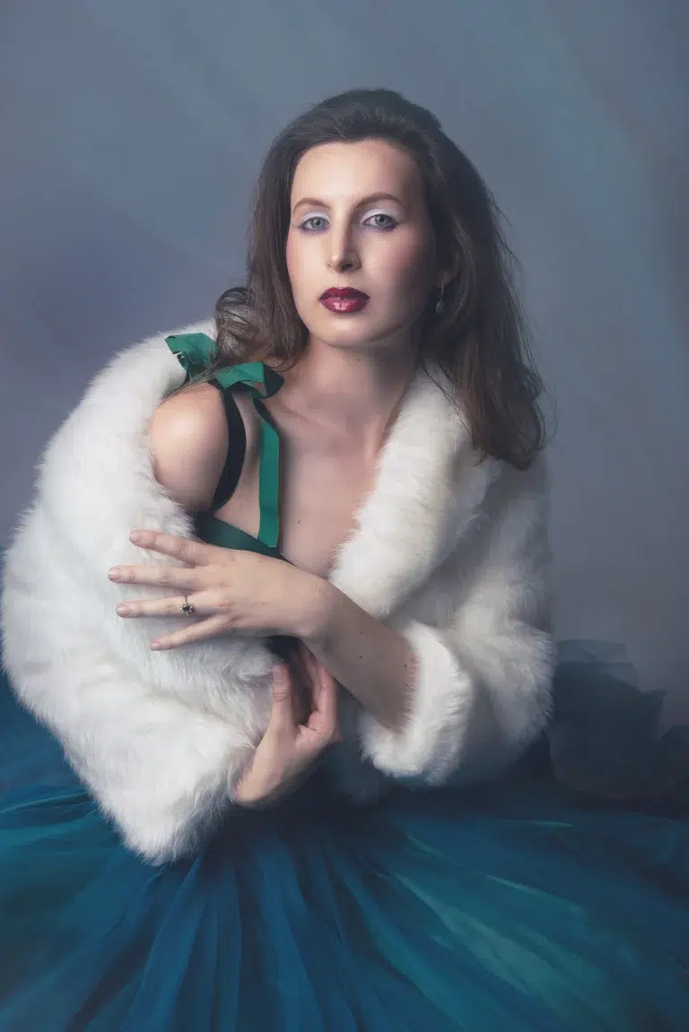 Artistic studio portrait of a woman in a white fur wrap and blue tulle dress with soft cinematic lighting.