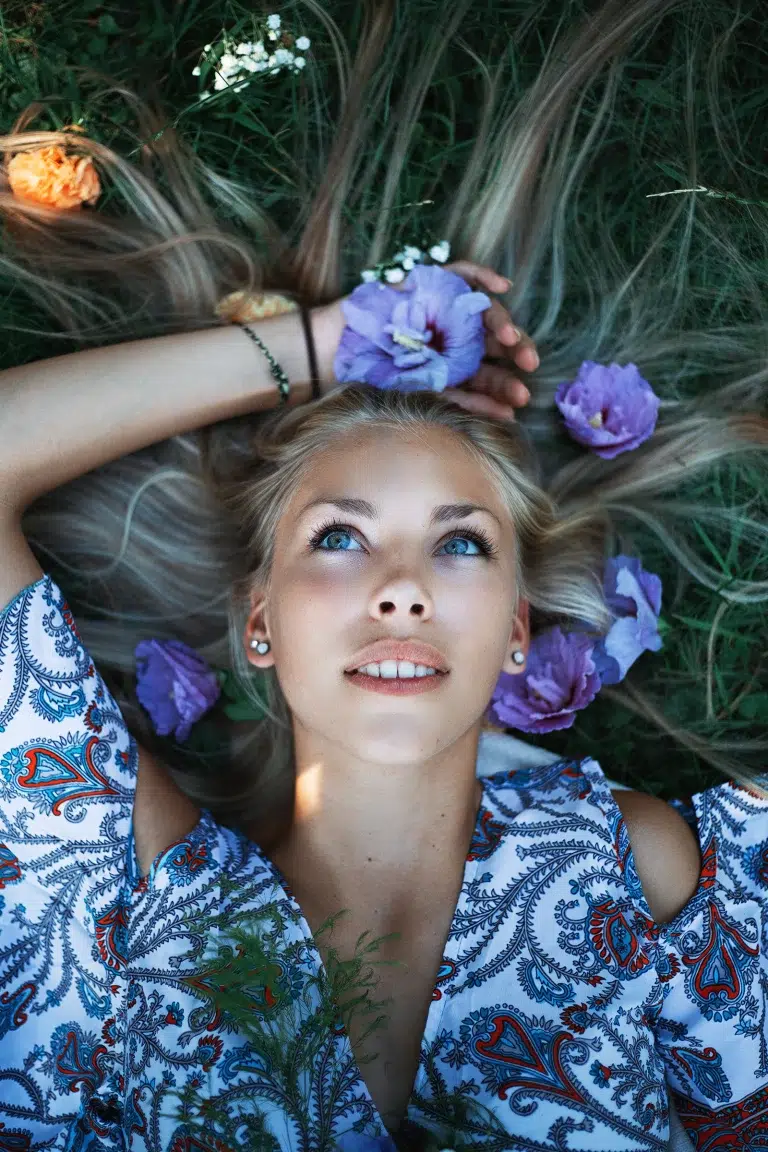 Woman lying on grass with purple flowers in her hair, photographed in natural light with beautiful color by Massen Photography Luxembourg.