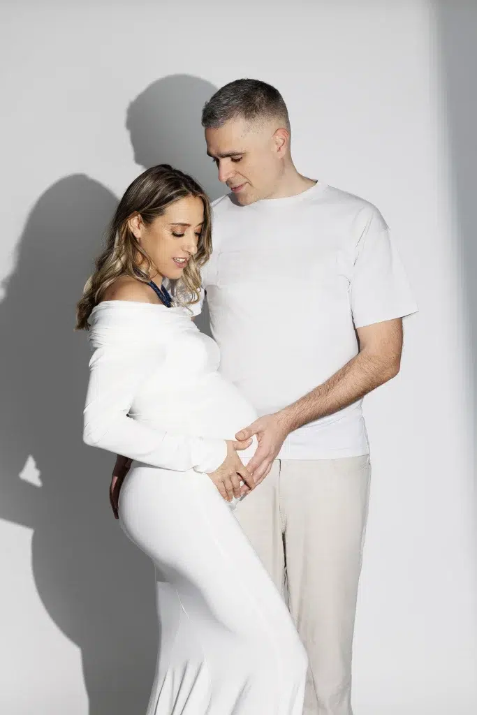 Maternity portrait of an expecting couple sharing a quiet moment in soft natural studio light in Luxembourg