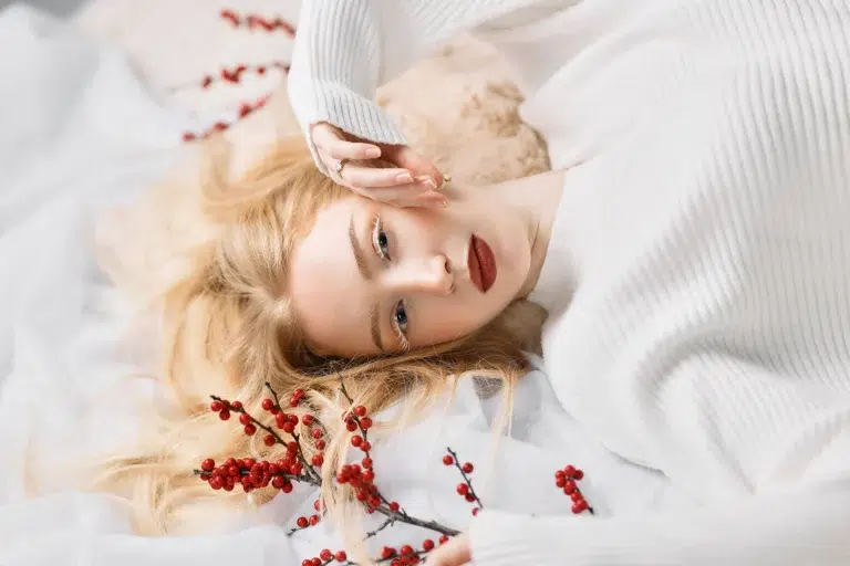 Soft winter beauty portrait of a blonde woman in a white sweater with red berries in Luxembourg
