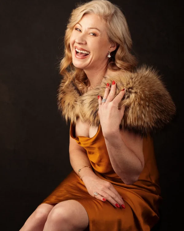 Joyful portrait of a mature woman in a golden satin dress with fur shawl, captured in a Luxembourg studio.