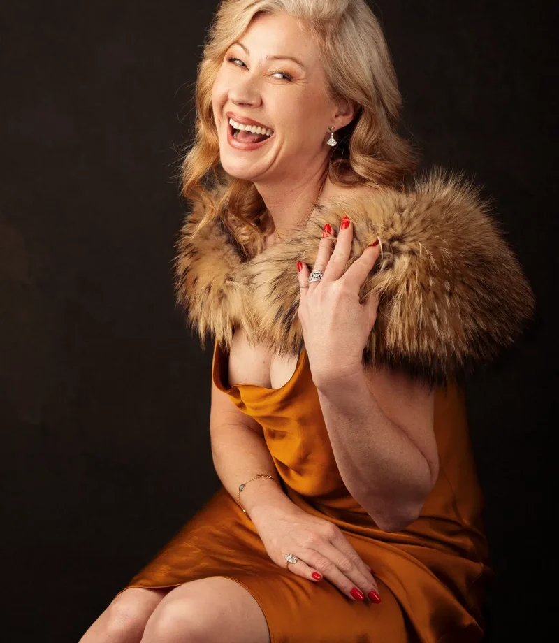 Joyful portrait of a mature woman in a golden satin dress with fur shawl, captured in a Luxembourg studio.