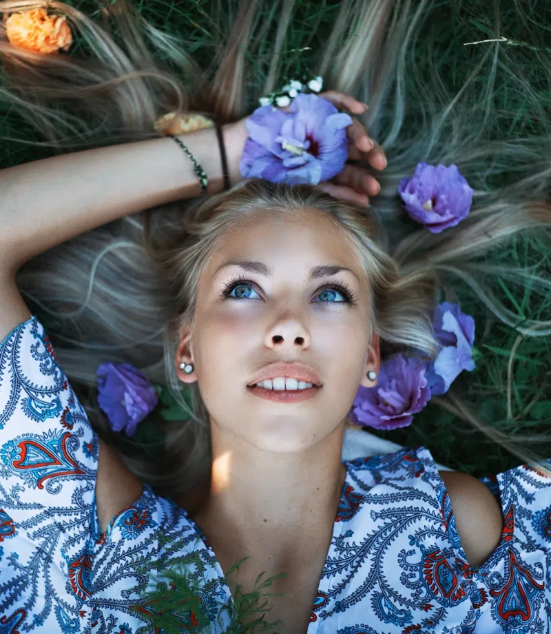 Woman lying on grass with purple flowers in her hair, photographed in natural light with beautiful color by Massen Photography Luxembourg.
