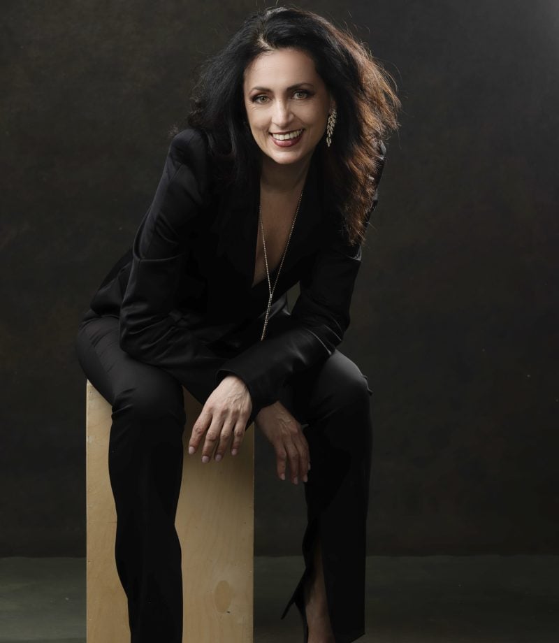 Stylish brunette woman in black suit smiling in professional studio