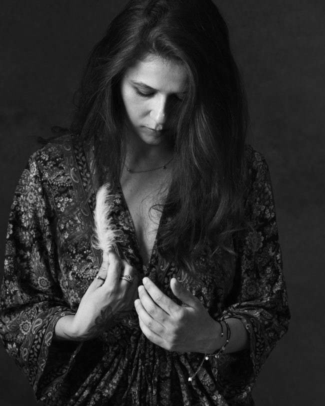 Woman in patterned robe holding a feather, looking down in black and white portrait